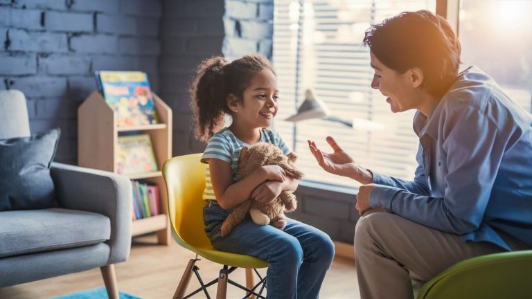 Psicólogo hablando con una niña en un entorno terapéutico, representando la psicología clínica.